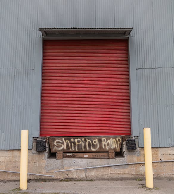 A worker wearing a dark grey shirt and or dark trousers is seen inside the back of a yellow flatbed truck, which is parked on a city street near a loading bay area for house removals. The worker is le