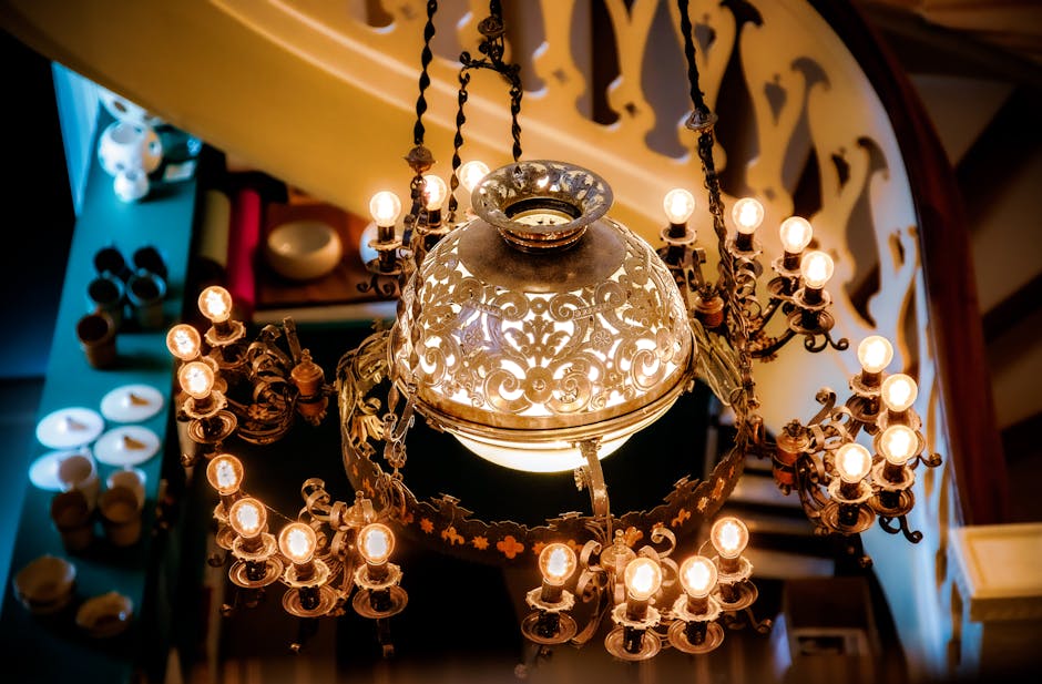 A close-up view of an ornate chandelier with multiple tiers of hanging crystal prisms and beads, suspended from a dark metal ceiling fixture. The chandelier is located inside a property, with warm lig